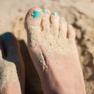 Teal-polished toes coated in sand on a beach - designed by Ace Web Design