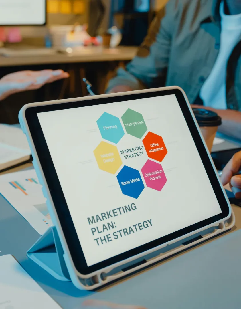 Tablet featuring marketing strategies, on a work surface, with people discussing marketing in the background